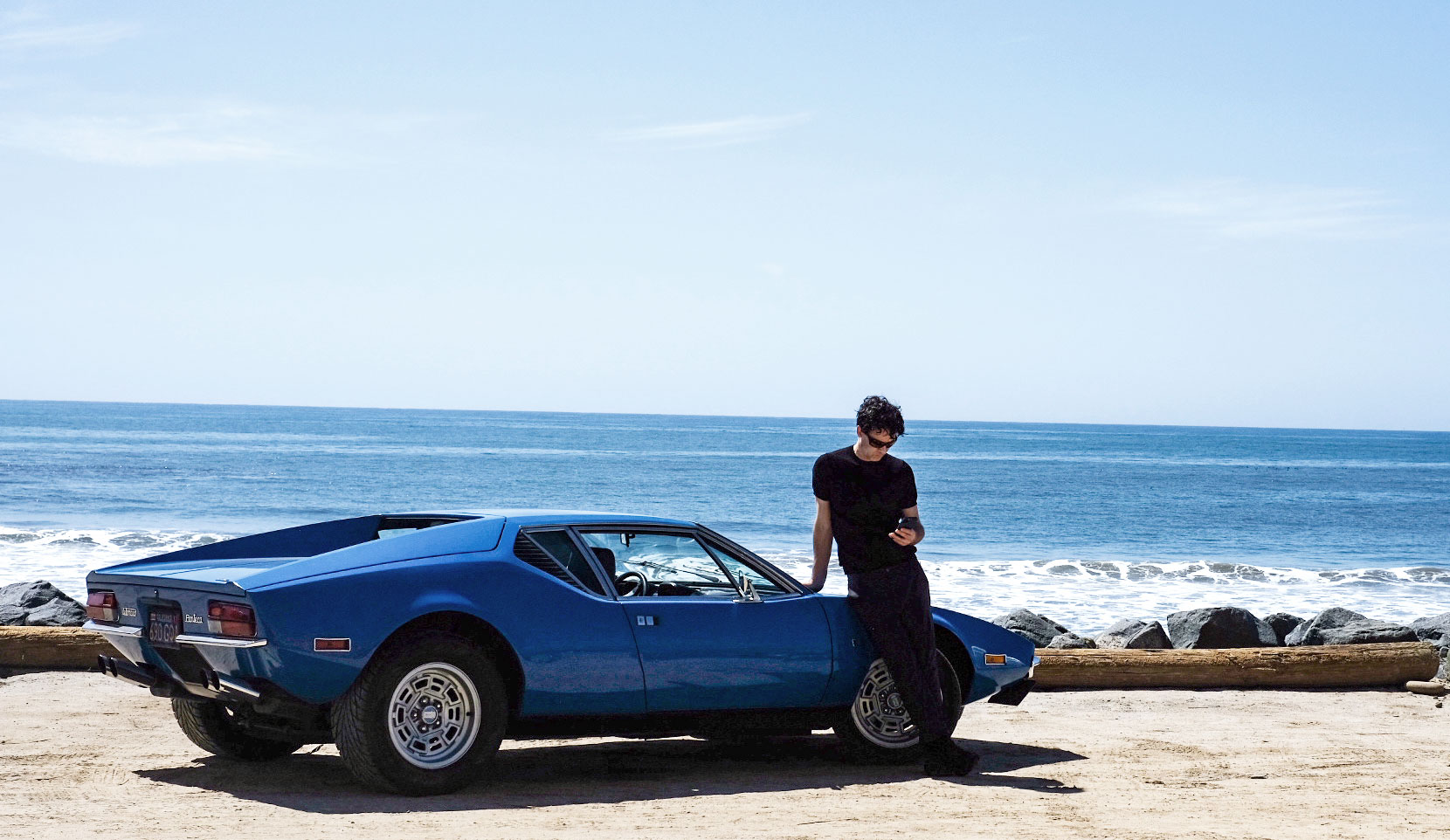 A man standing beside a blue Pantera on the coast